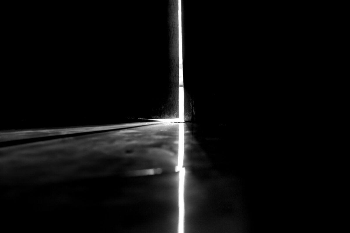 Light enters through the gaps in the door in a dark room